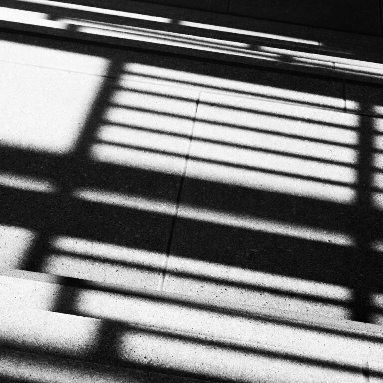 Black and white abstract: the shadow of a railing falling in diagonal stripes across a wall