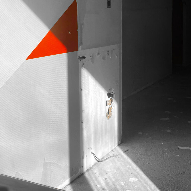 Red and orange triangle of light on a bare wall beside an open doorway