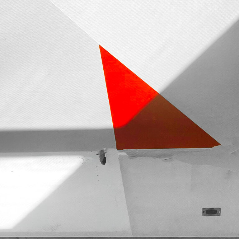 Red triangle of light meeting a diagonal shadow on a white wall
