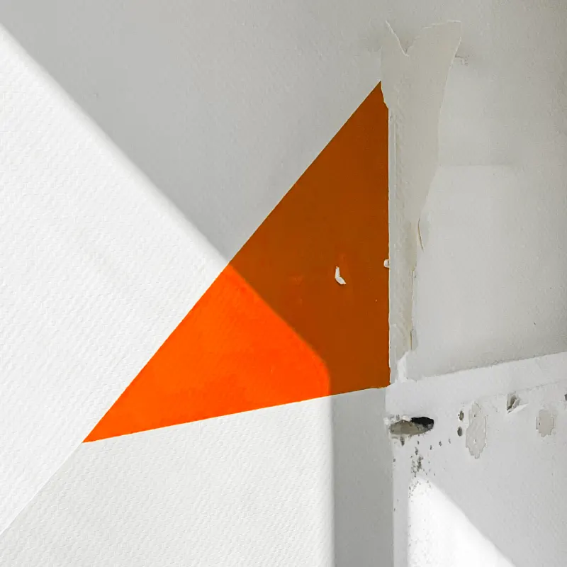 A single orange triangle of paint on a white interior wall — from the Abstract series